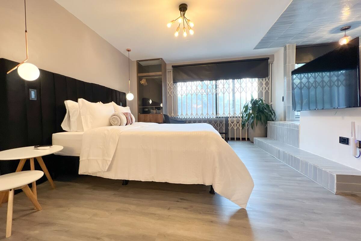 Ett modernt hotellrum med en stor säng, ett litet sidobord, en spegel och utsikt över omgivningarna.