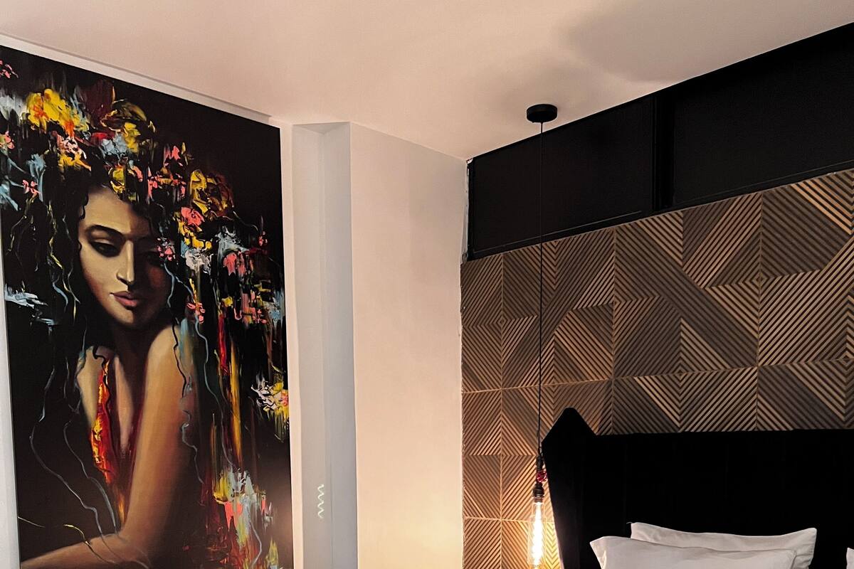 Ett hotellrum med en stor säng, ett modernt sänggavel och en färgstark, abstrakt målning på väggen.