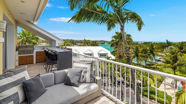 A balcony with a sofa, a grill, and a view of a beach and palm trees. - Oceanview Luxury 3 Bed Penthouse 5 minute walk to Grace Bay Beach (Providenciales)