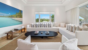 A modern living room with a large flat-screen TV, a black coffee table, and a white sofa with multiple cushions. - Oceanview Luxury 3 Bed Penthouse 5 minute walk to Grace Bay Beach (Providenciales)