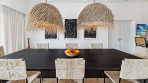A dining area with a dark wooden table, woven chairs, and a fruit bowl centerpiece. - Oceanview Luxury 3 Bed Penthouse 5 minute walk to Grace Bay Beach (Providenciales)