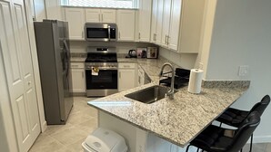 Una cocina moderna con armarios blancos, electrodomésticos de acero inoxidable, encimera de granito y un cubo de basura pequeño.