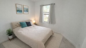 A bedroom with a bed, a bedside table, a lamp, a window with curtains, and two wall-mounted pictures. - Modern Villa New Build & Furniture/Resorts Amenities (Bradenton)