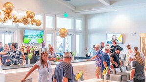 A bar area with a counter, seating, and a television screen displaying a golf channel. - Modern Villa New Build & Furniture/Resorts Amenities (Bradenton)