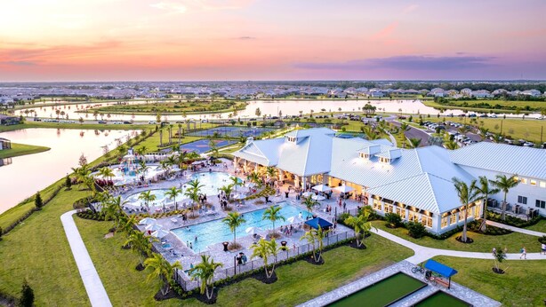 Un resort con múltiples piscinas, un edificio grande con techo azul y un lago al fondo.