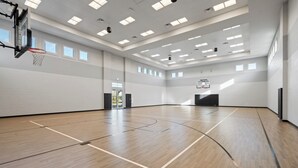 Una amplia cancha de baloncesto cubierta con suelo de madera, múltiples aros y tragaluces que dejan entrar luz natural.