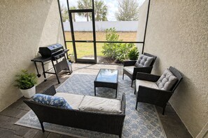A patio with wicker furniture, a grill, and a view of the yard.
