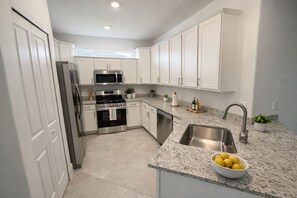 Une cuisine moderne avec des meubles blancs, des appareils en acier inoxydable, un plan de travail en granit et un bol de citrons.