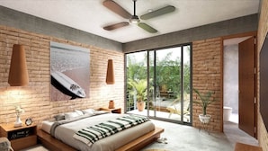 Een moderne slaapkamer met een groot bed, een plafondventilator, een bakstenen muur en uitzicht op groen.