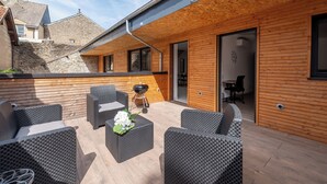 Un patio extérieur couvert, aménagé avec des meubles en osier et doté d’un barbecue.
