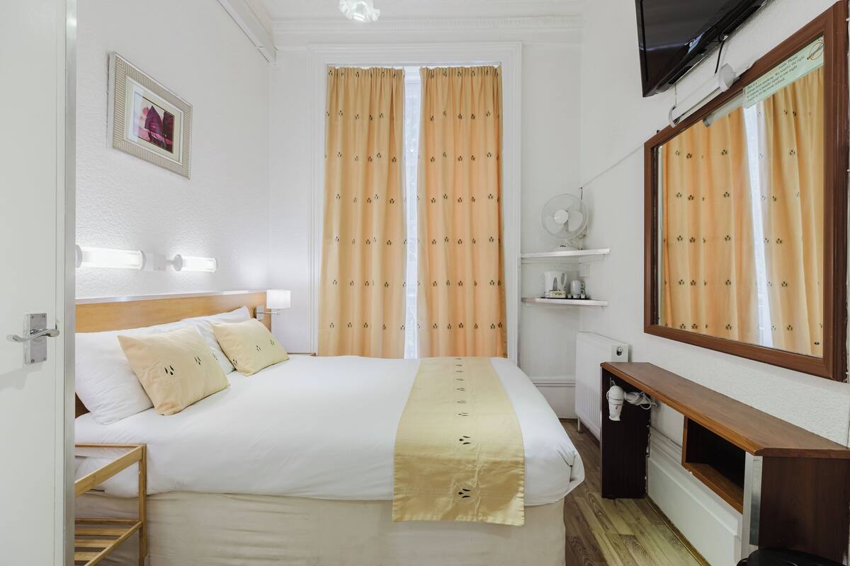 A hotel room with a bed, bedside table, mirror, and a television.