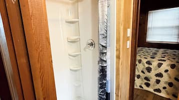 A bathroom with a shower, a toilet, and a sink. There is a wooden door frame and a window with blinds.