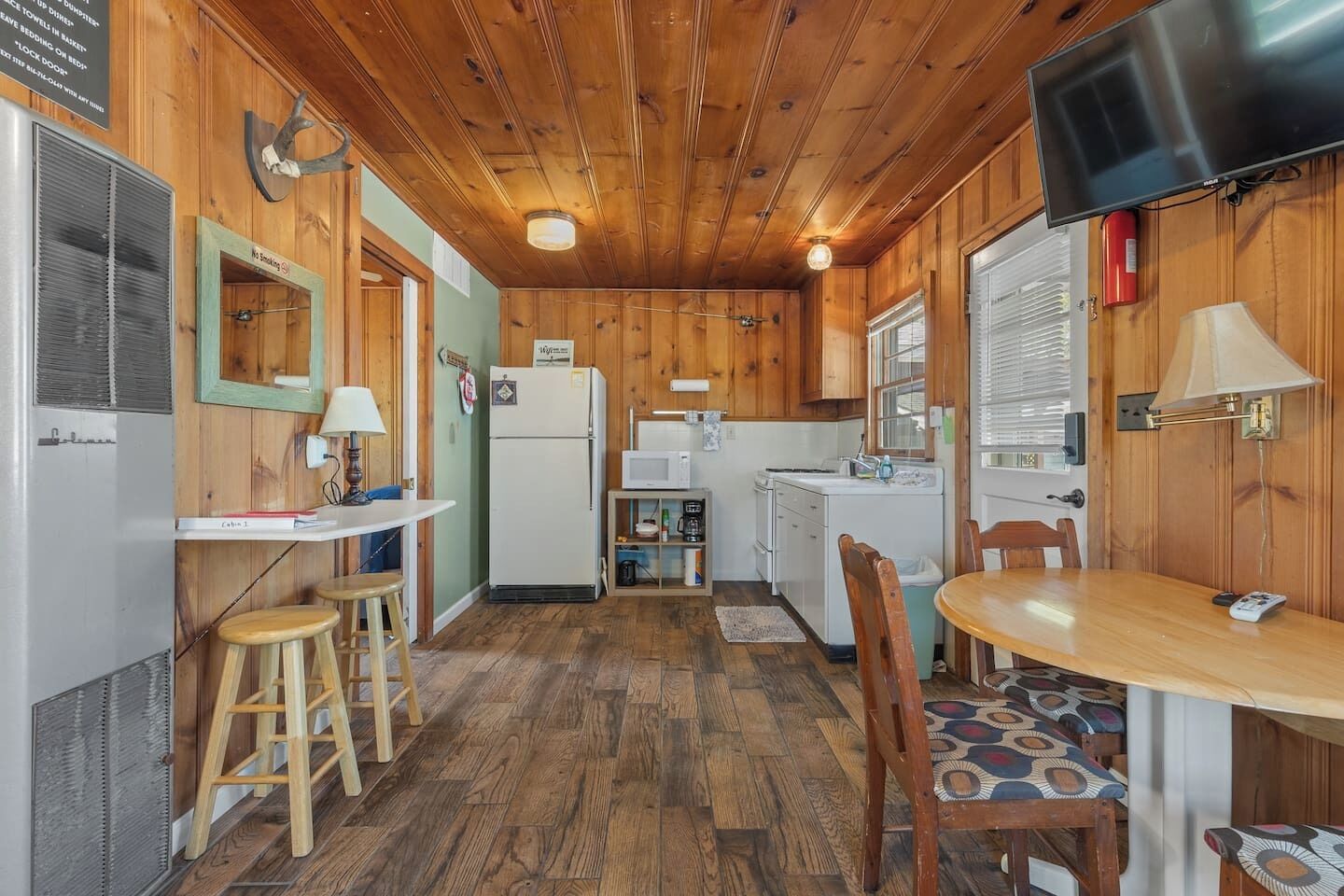 A compact kitchen with a refrigerator, microwave, and stove. There is a dining table with chairs and a small stool.