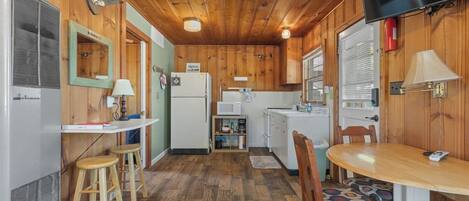 A compact kitchen with a refrigerator, microwave, and stove. There is a dining table with chairs and a small stool.