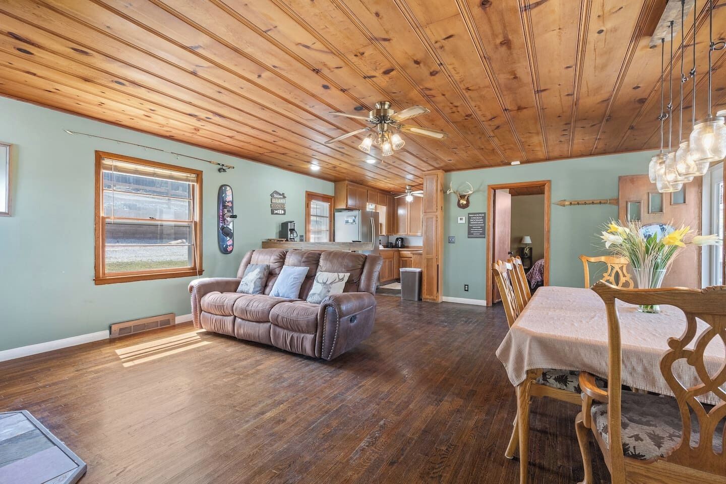 A spacious living room with a leather sofa, wooden dining table, and a ceiling fan.