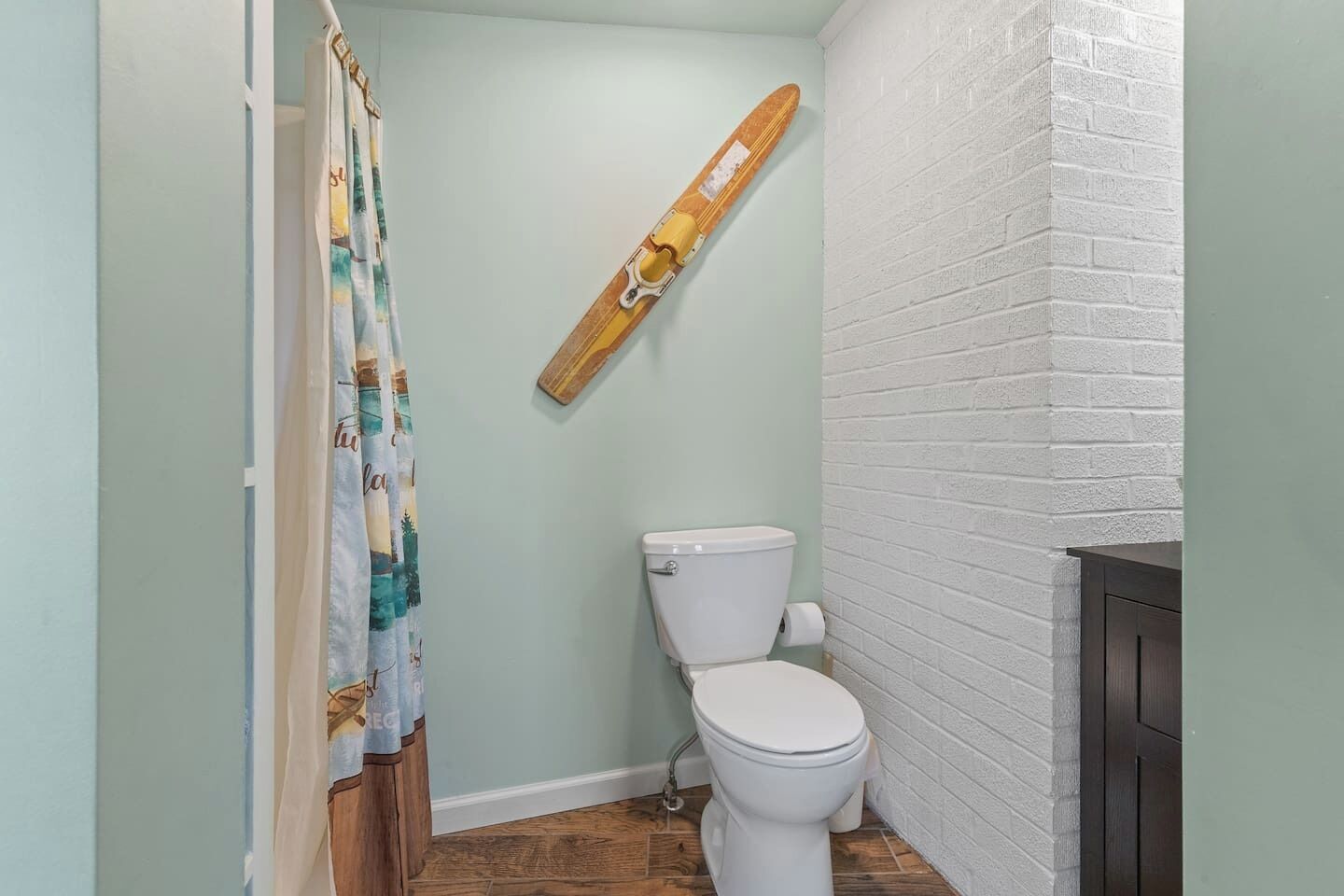 A bathroom with a toilet, a shower curtain, and a skateboard hanging on the wall.
