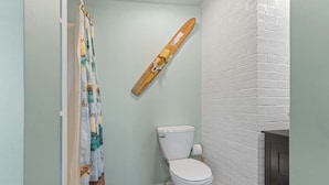 Un baño con inodoro, cortina de ducha y una patineta colgada en la pared.