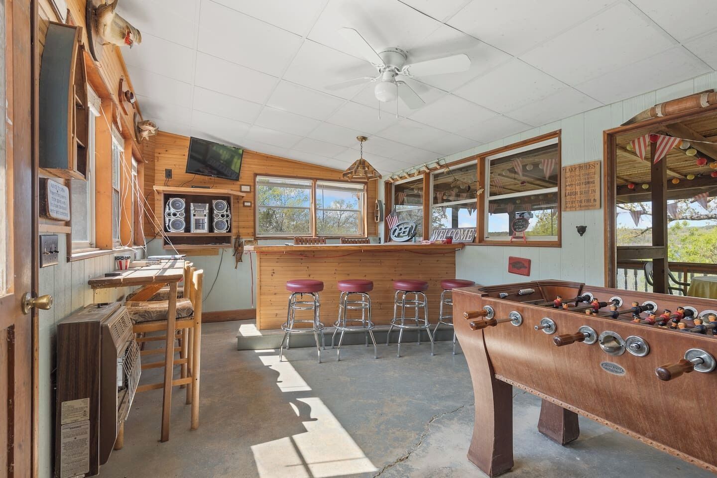A room with a foosball table, bar stools, a television, and wooden walls.