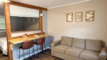 A compact living space with a wooden desk, two chairs, a sofa, and a bed.