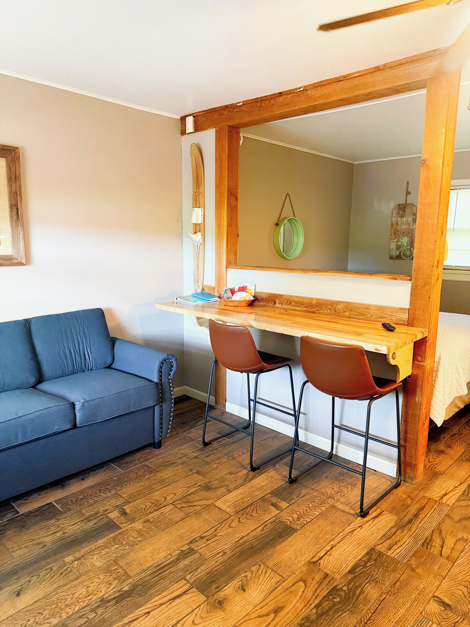 A compact room with a wooden desk, two chairs, a sofa, and a mirror.