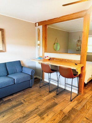 A compact room with a wooden desk, two chairs, a sofa, and a mirror.