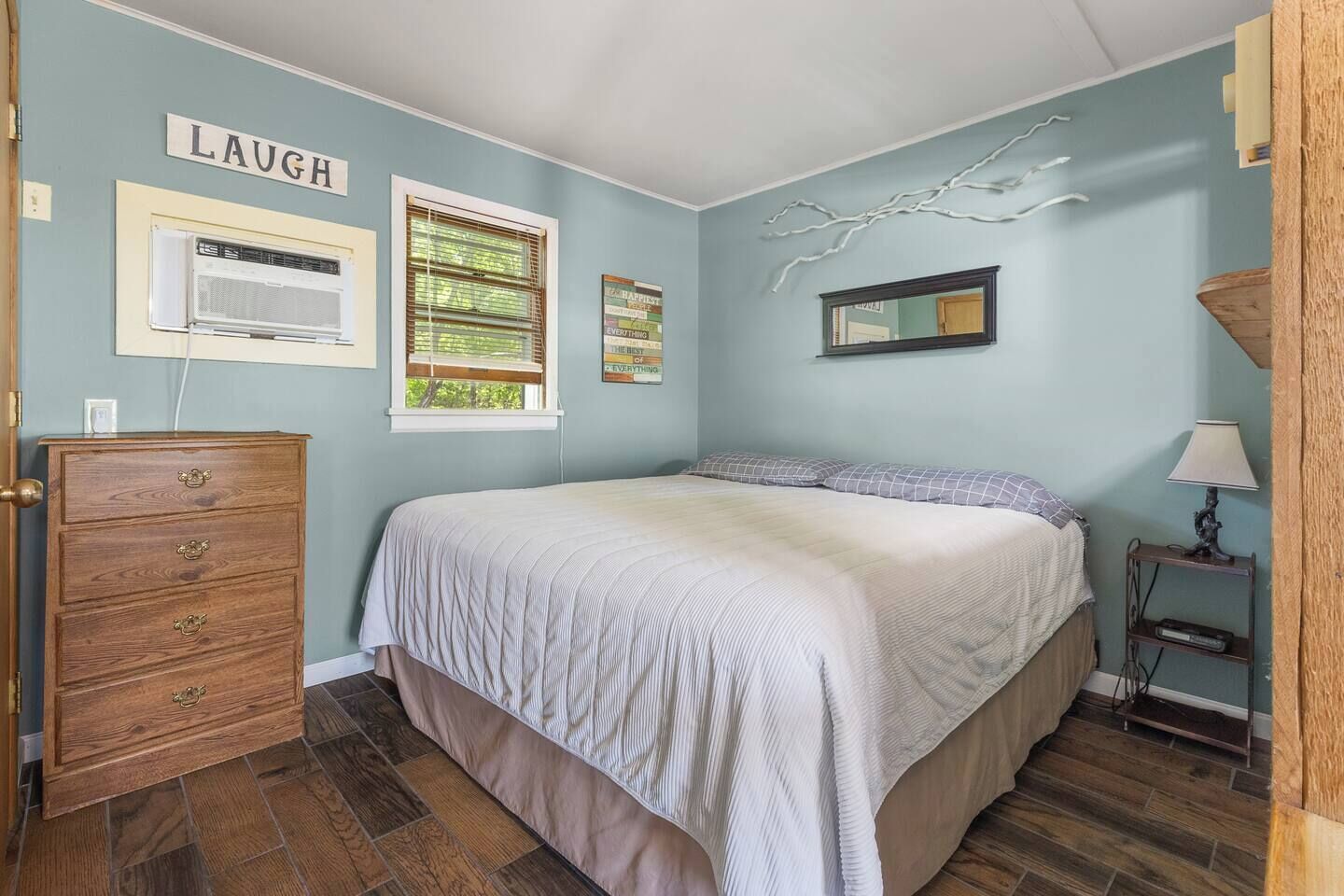 A bedroom with a bed, dresser, and wall decorations including a sign that says 'LAUGH'.