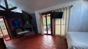 Ein Zimmer mit rotem Fliesenboden, einem Bett, einer Bank, einem Fernseher und einer zur Außenseite führenden Tür.