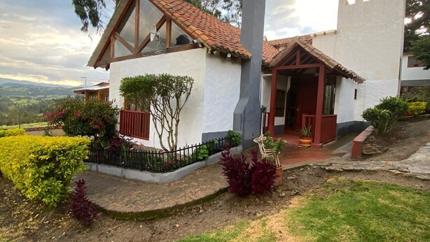Ein modernes Haus mit weißer Fassade, einem Ziegeldach und einem kleinen Garten mit verschiedenen Pflanzen und Sträuchern.
