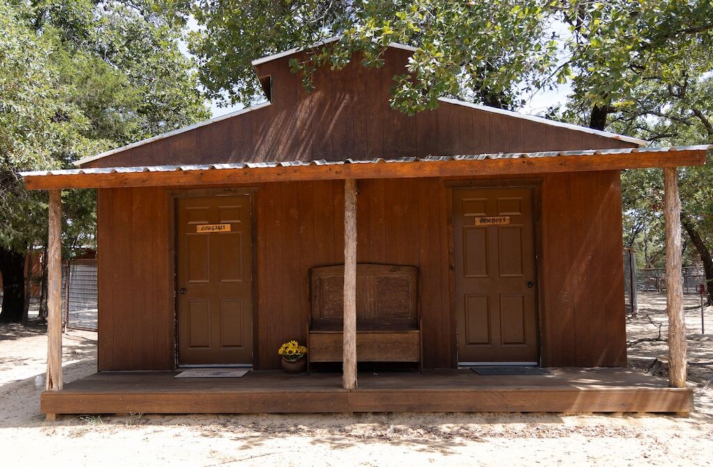 A rustic wooden cabin with two doors, a bench, and a small table with flowers.