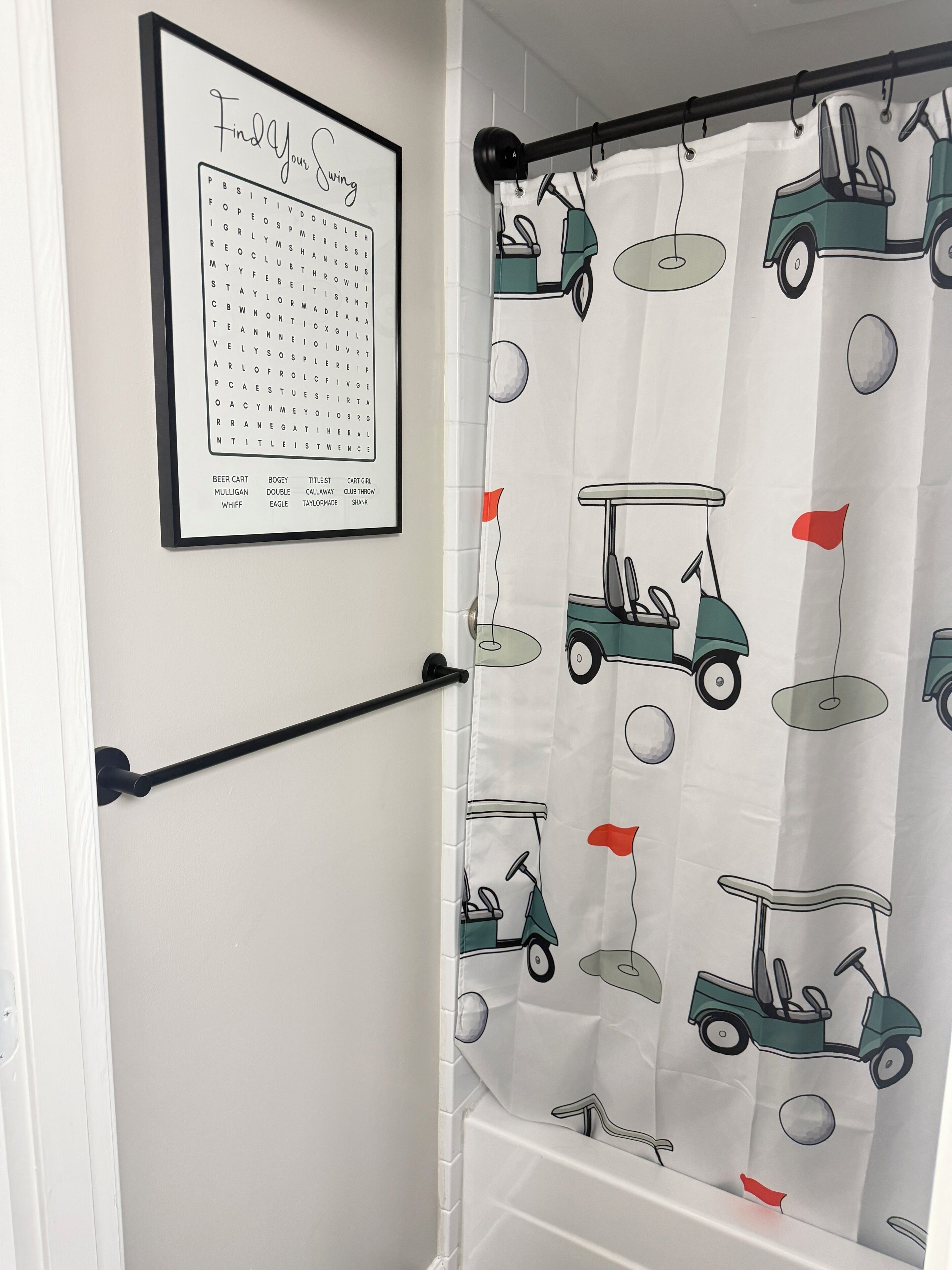 Un baño con cortina de ducha con motivos de golf, un rompecabezas de búsqueda de palabras enmarcado en la pared y un perchero.