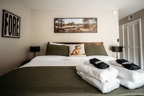 A hotel room with a bed, pillows, a painting, a door, and towels.