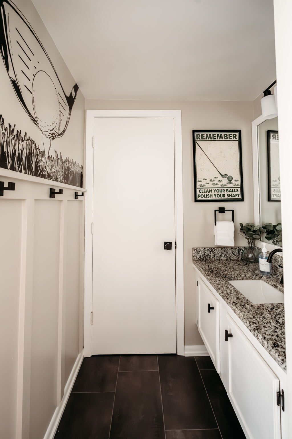 Un baño con puerta blanca, un lavamanos con encimera de granito, un espejo y un cartel en la pared.