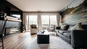 Una sala de estar moderna con chimenea, un televisor de pantalla plana grande, un sofá, una mesa de centro y un mural en la pared.