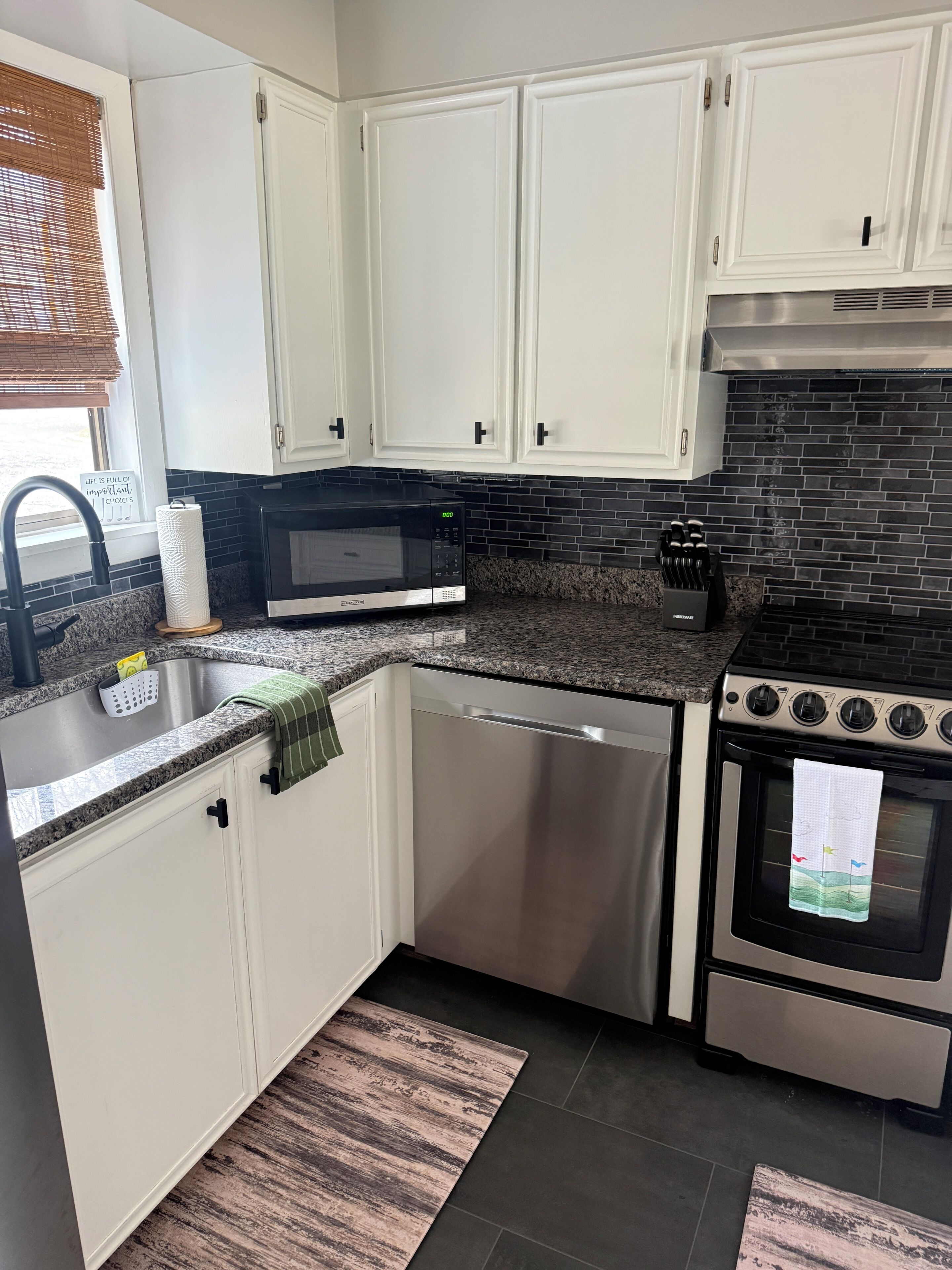 A kitchen with white cabinets, a black microwave, a stainless steel dishwasher, and an oven with a towel hanging on the door.