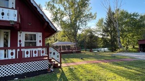 A red building with a white lattice fence, a covered outdoor seating area, and a grassy yard.