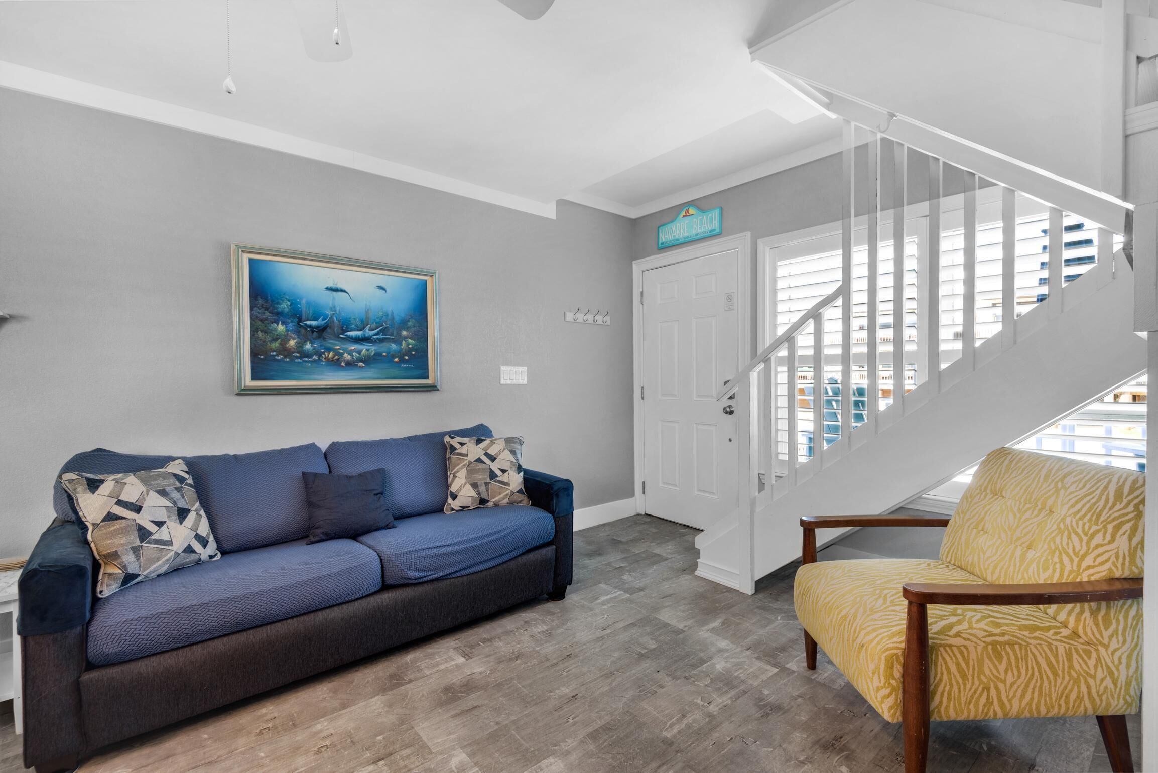 A living room with a blue sofa, a yellow armchair, a painting, and a staircase.