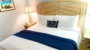 Un llit ben fet amb una manta blava, un coixí amb el text “Jail away”, una làmpada de nit i una petita taula de nit de fusta amb un telèfon.