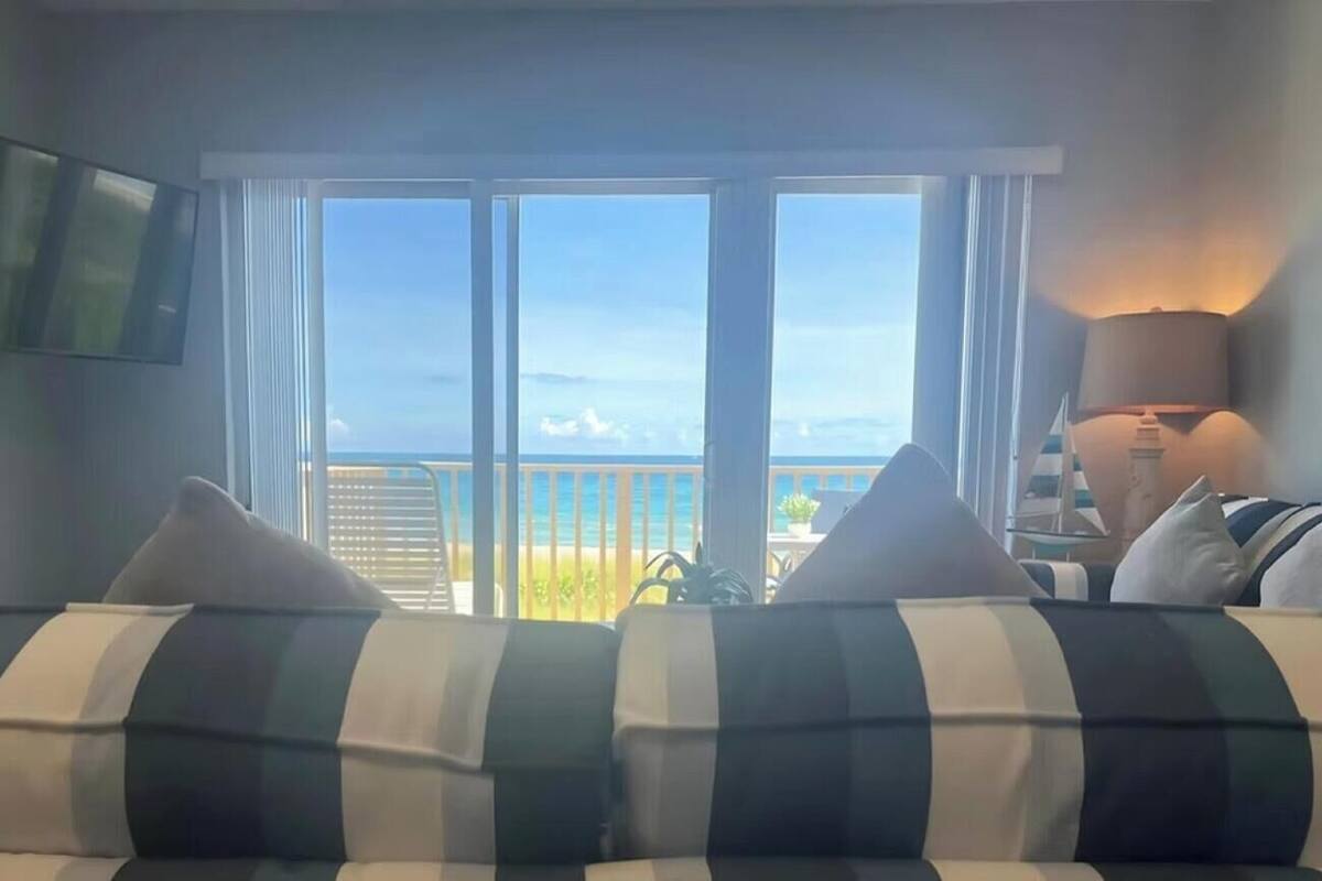 A room with a large window offering a view of the beach and ocean.