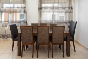 Un espace repas comprenant une table et des chaises, des rideaux légers et un sol carrelé.