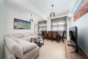 Un salon comprenant un canapé, une table basse, une table à manger avec des chaises, un téléviseur et des œuvres d’art accrochées aux murs.
