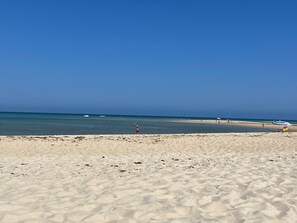 Uma praia com céu claro, águas calmas e alguns barcos.
