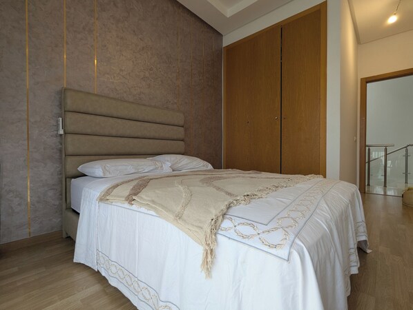A bedroom with a large bed, wooden wardrobe, and a staircase.