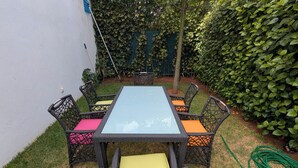 Una mesa rectangular con cubierta de vidrio y sillas de mimbre, cada una con cojín.