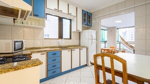 A modern kitchen with a microwave, stove, and refrigerator. There is a dining area with a table and chairs. - Apt w/ Balcony & BBQ 290m From the sea Cau0199 (Itapema)