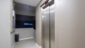 A narrow hallway with a trash bin, a digital display, and a metallic elevator door. - Apt w/ Balcony & BBQ 290m From the sea Cau0199 (Itapema)