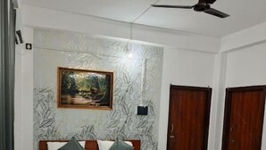 A bedroom with a bed, a ceiling fan, a painting on the wall, and wooden doors. - Rudra homes (Guwahati)