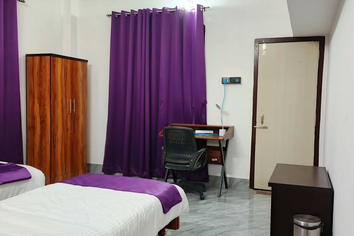 A bedroom with two beds, a desk, a chair, a wardrobe, a ceiling fan, and a door.