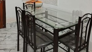 A dining area with a glass table and metal chairs, a small sink, and a decorative plate on the wall. - Rudra homes (Guwahati)