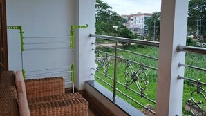 A balcony with wicker furniture, a metal railing, and a view of a building and greenery.