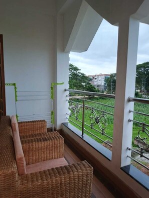 A balcony with wicker furniture, a metal railing, and a view of a building and greenery.